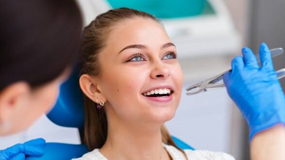 Woman in dental chair as dentist holds forceps