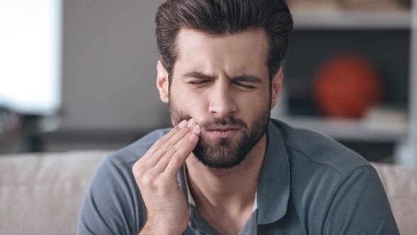Man in gray polo shirt touching his cheek in pain